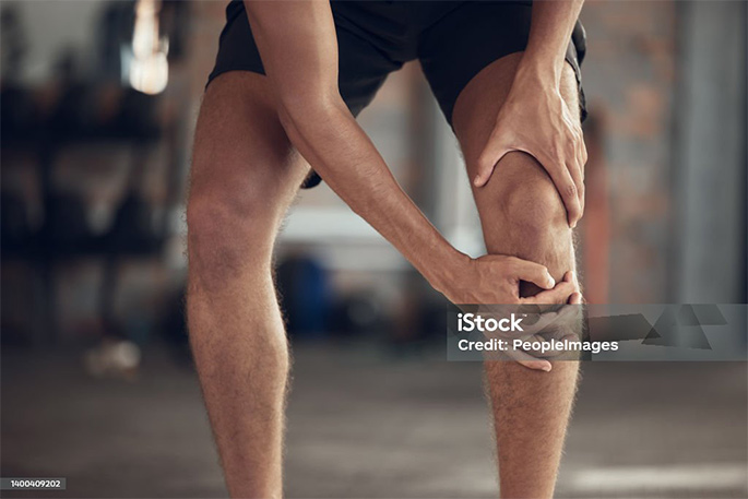 Picture of Closeup of athlete knee joint pain. Hands of fit man touching his knee in pain. Strong man with a sore knee in the gym. Bodybuilder with a hurt knee injury. Active man with a knee sprain