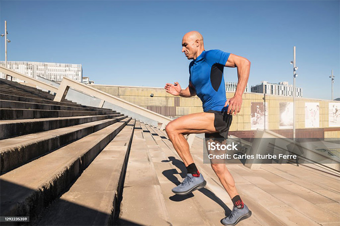 Picture of Profile of a man with shaved head and sportswear running up stairs in an urban park of a city