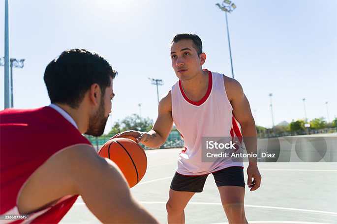 Picture of Young men playing street basketball outdoors, dribbling ball on court, enjoying workout and competition