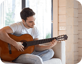 A man on a couch skillfully playing an acoustic guitar, showcasing his hands.
